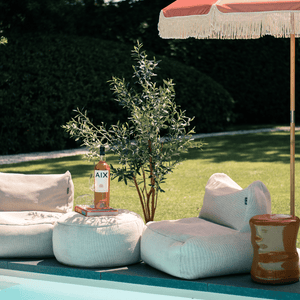Kunstolijfboom 'Sophia' van 165 cm hoog, gepresenteerd in een zomerse setting met een zwembad. De boom, met zes houten stammen en 1768 levensechte polyester bladeren, voegt een elegante mediterrane flair toe aan de buitenruimte, naast het verfrissende zwembad. De foto benadrukt de stijlvolle uitstraling en de geschiktheid van de kunstolijfboom voor een zomerse tuin of terras.