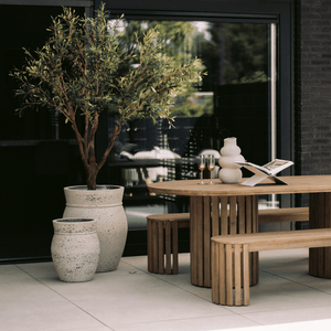 Kunstolijfboom 'Verdi' van 200 cm hoog, geplaatst onder een veranda. De foto toont de kunstboom met zijn 3366 levensechte bladeren, realistische glasvezel stam, en houten takken, die een luxe mediterrane sfeer toevoegen aan de veranda. De setting benadrukt de indrukwekkende hoogte en elegante uitstraling van de kunstolijfboom in een sfeervolle buitenruimte.